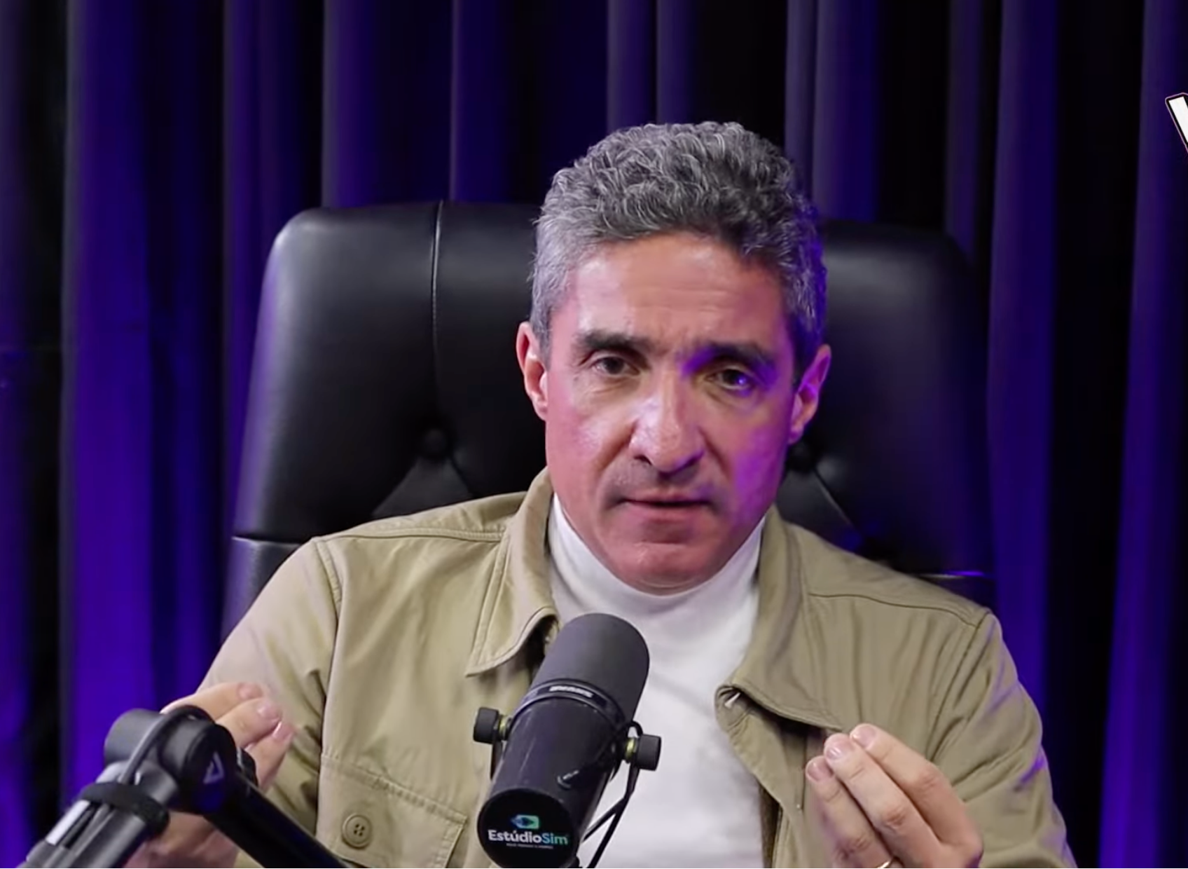 Um homem está sentado em uma cadeira em frente a um microfone.