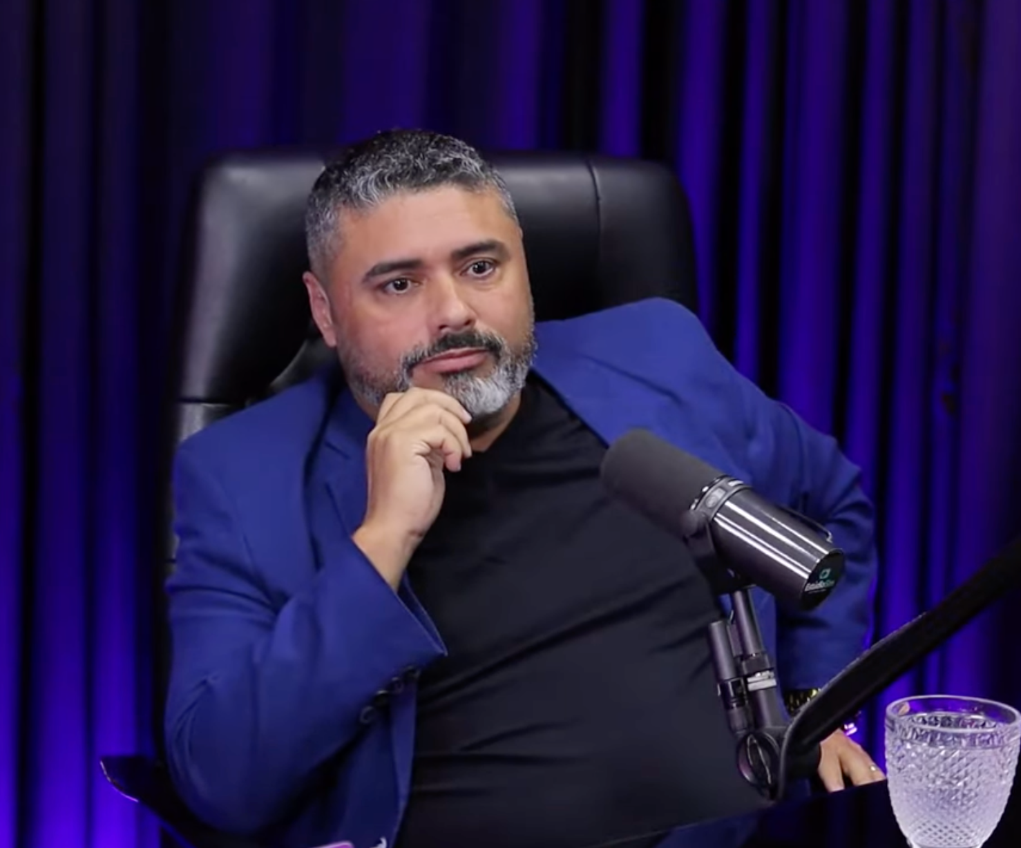 Um homem de terno azul está sentado em frente a um microfone.