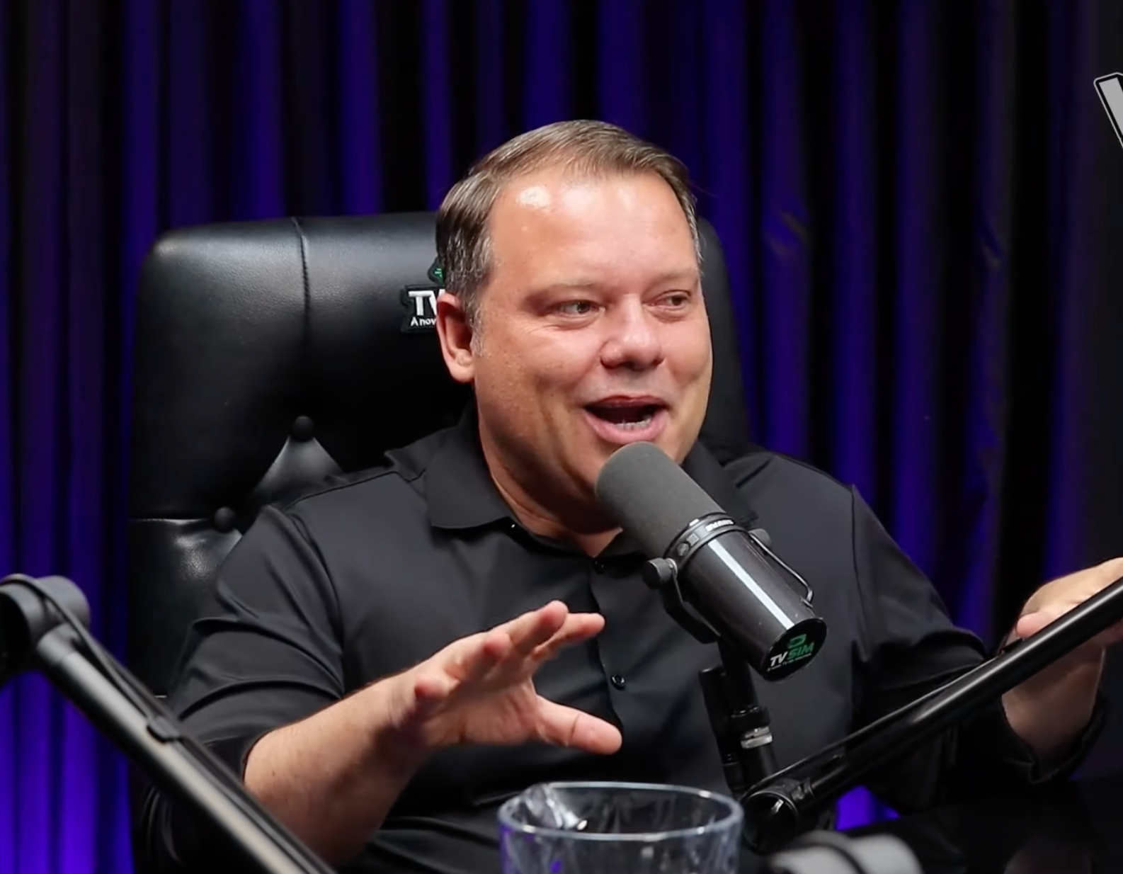 Um homem está sentado em uma cadeira em frente a um microfone.