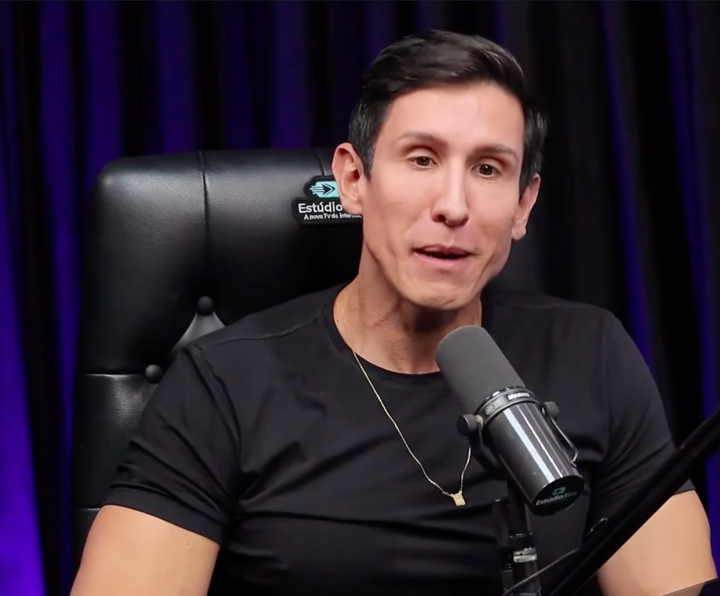 Um homem de camisa preta está sentado em frente a um microfone