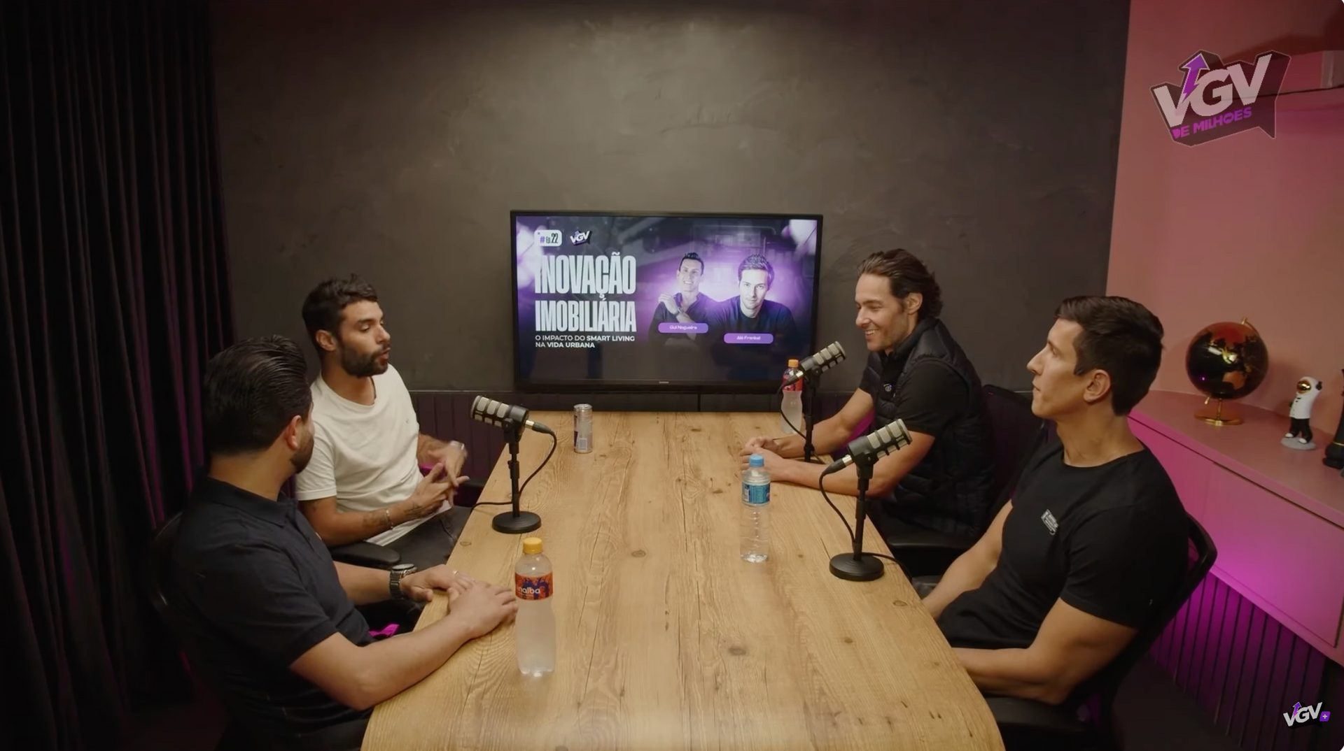 Um grupo de homens está sentado ao redor de uma mesa com microfones.