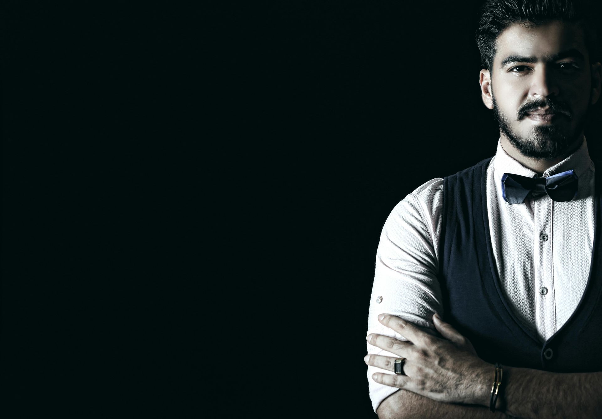 A man with a beard and bow tie is standing with his arms crossed.