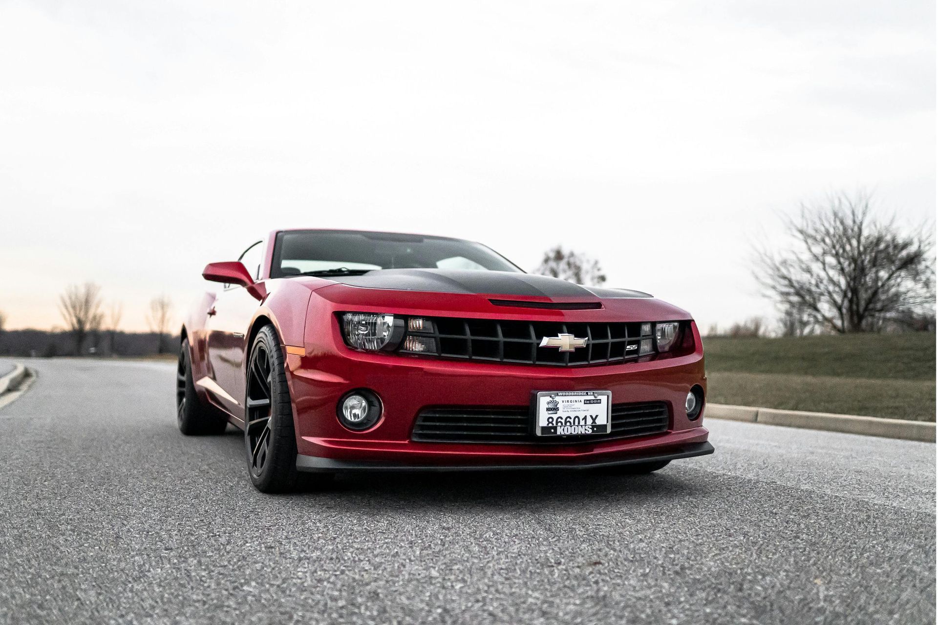 Red Chevrolet Camaro sports car on a paved road with a black hood stripe, daytime.