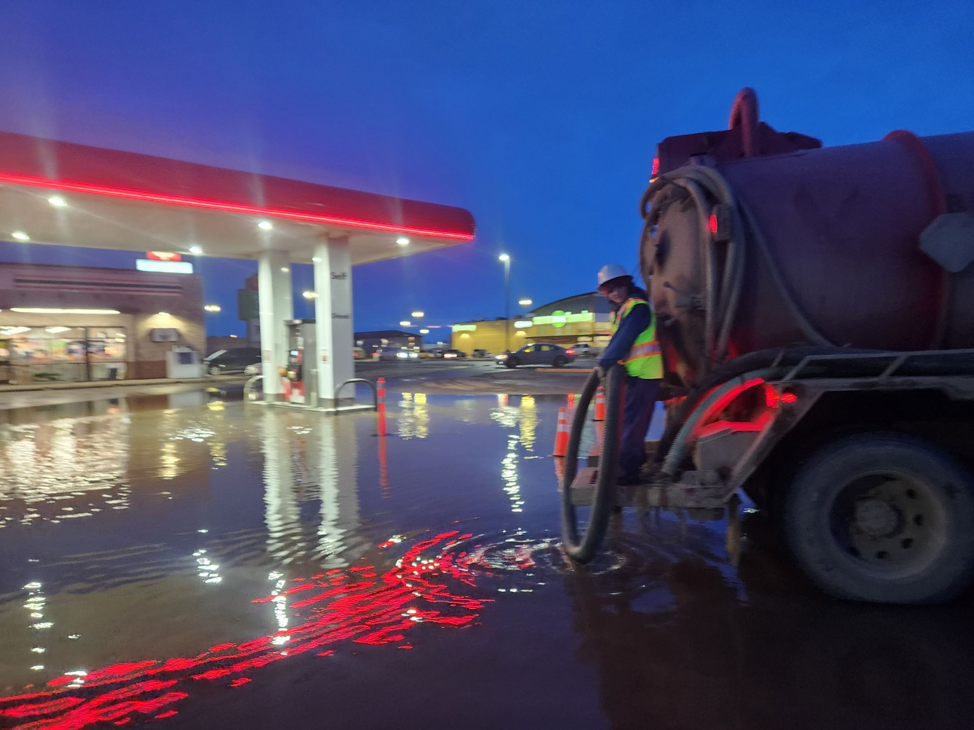 A man is pumping water from a truck at a flooded gas station