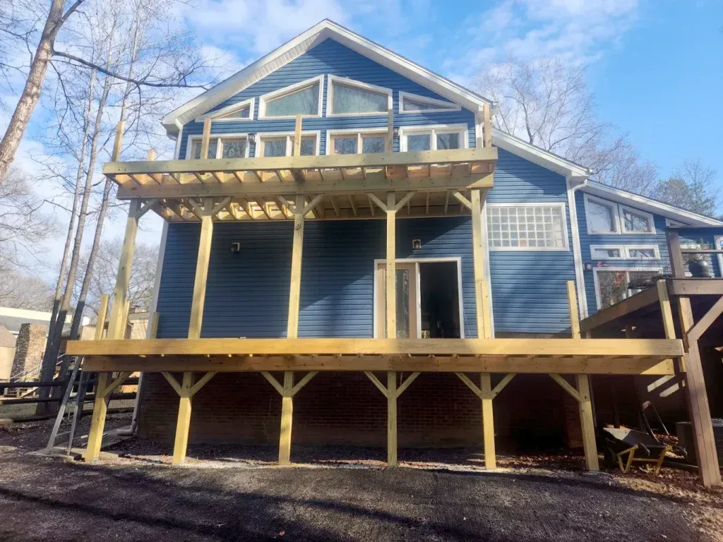 Blue house with a large wooden deck and pergola. Bright blue sky overhead.