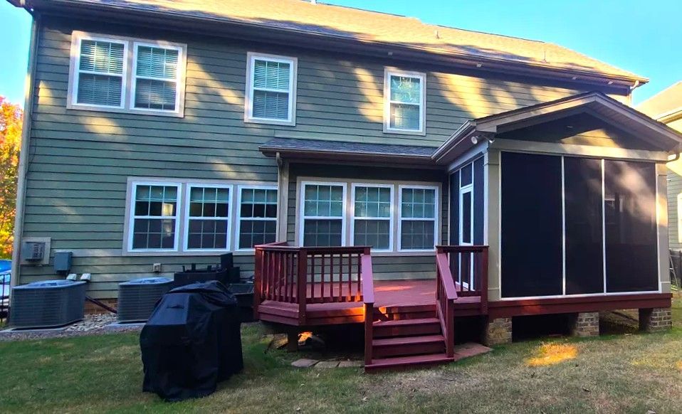 Back of a two-story green house with a red deck and a screened-in porch; set on a grassy lawn.