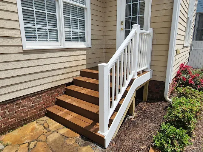 Wooden steps with white railing lead up to a door on a house with beige siding.
