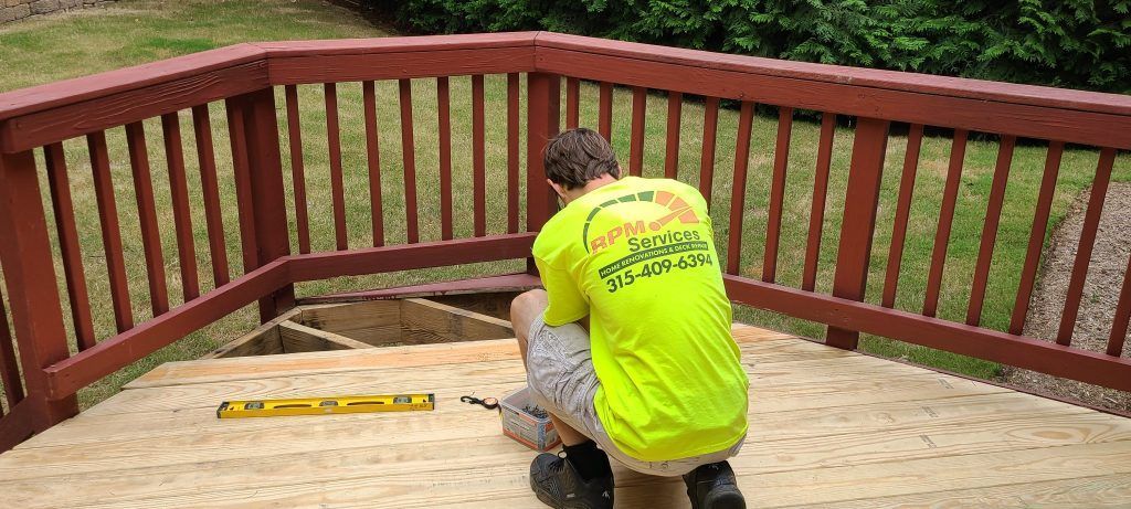 Person in a neon green shirt working on a wooden deck, surrounded by a red railing, with tools and a level visible.