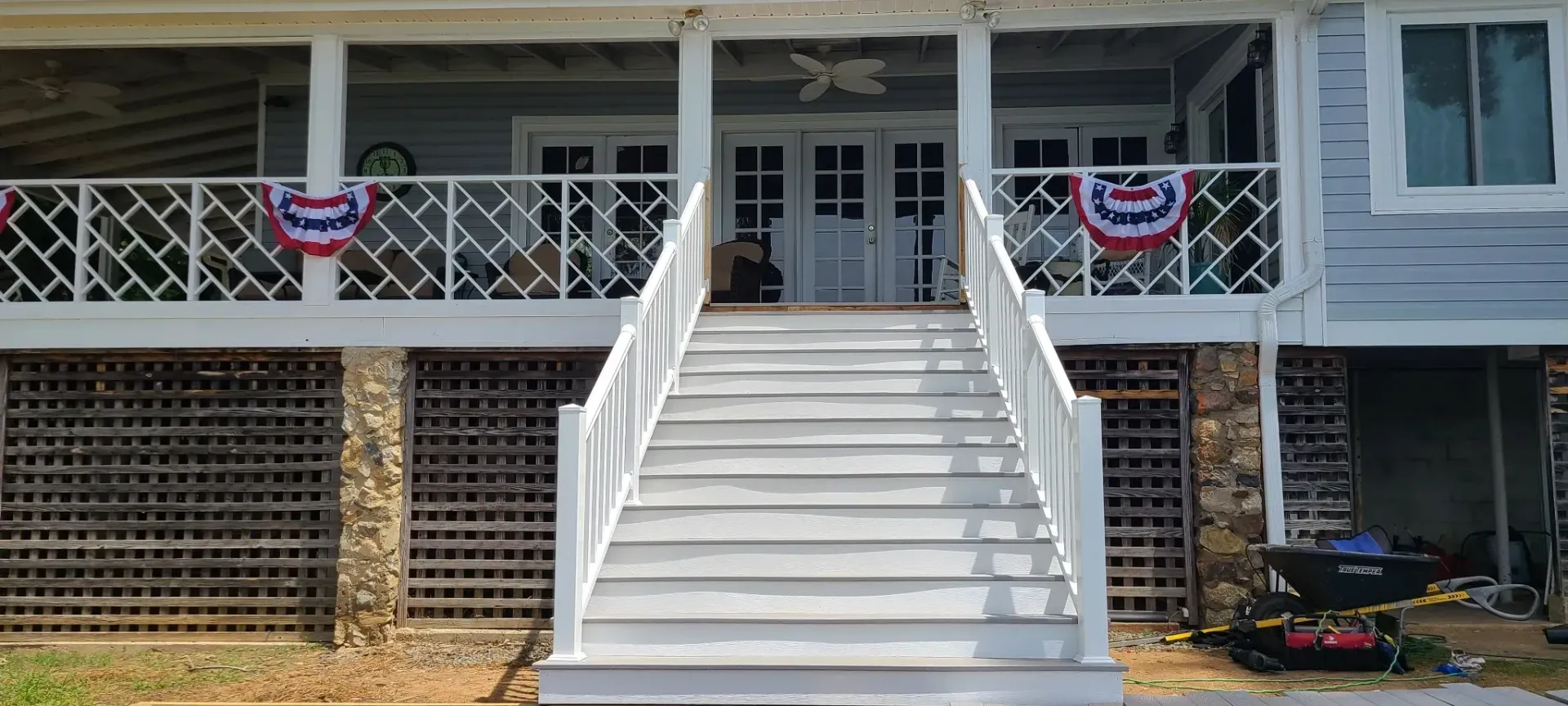 A white-painted house with a porch and stairs. Patriotic bunting hangs on the porch railing.