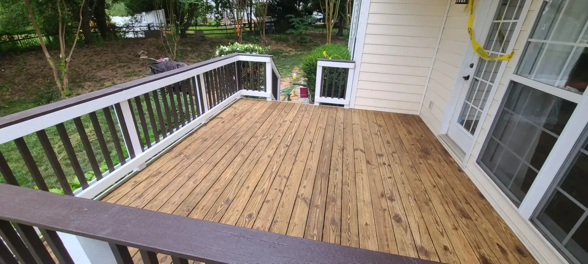 A wooden deck with white and brown railings next to a house with white siding and glass doors.