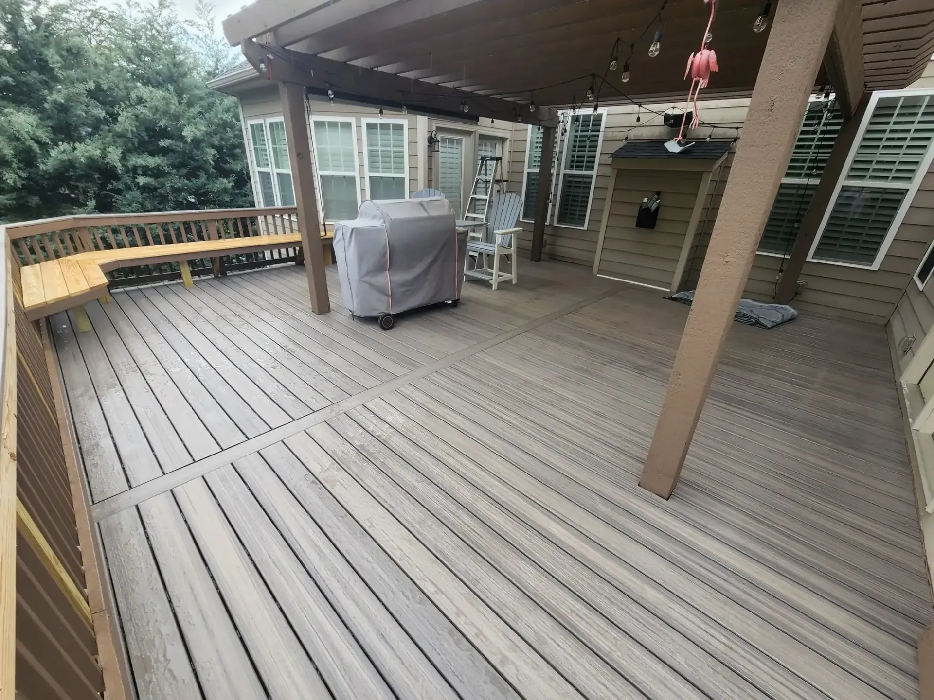 A spacious wooden deck with a covered seating area, featuring a grill and surrounding house with windows.