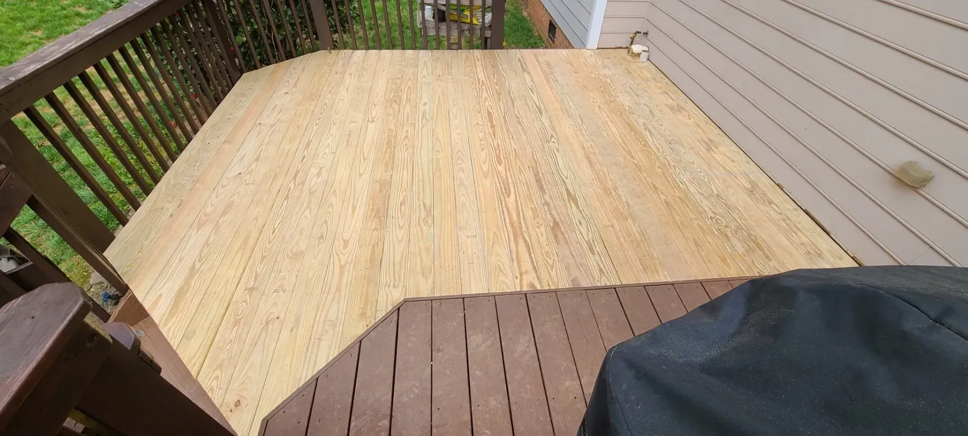 A wooden deck with new plywood laid on top. The deck is outdoors, and a grill cover is in the foreground.