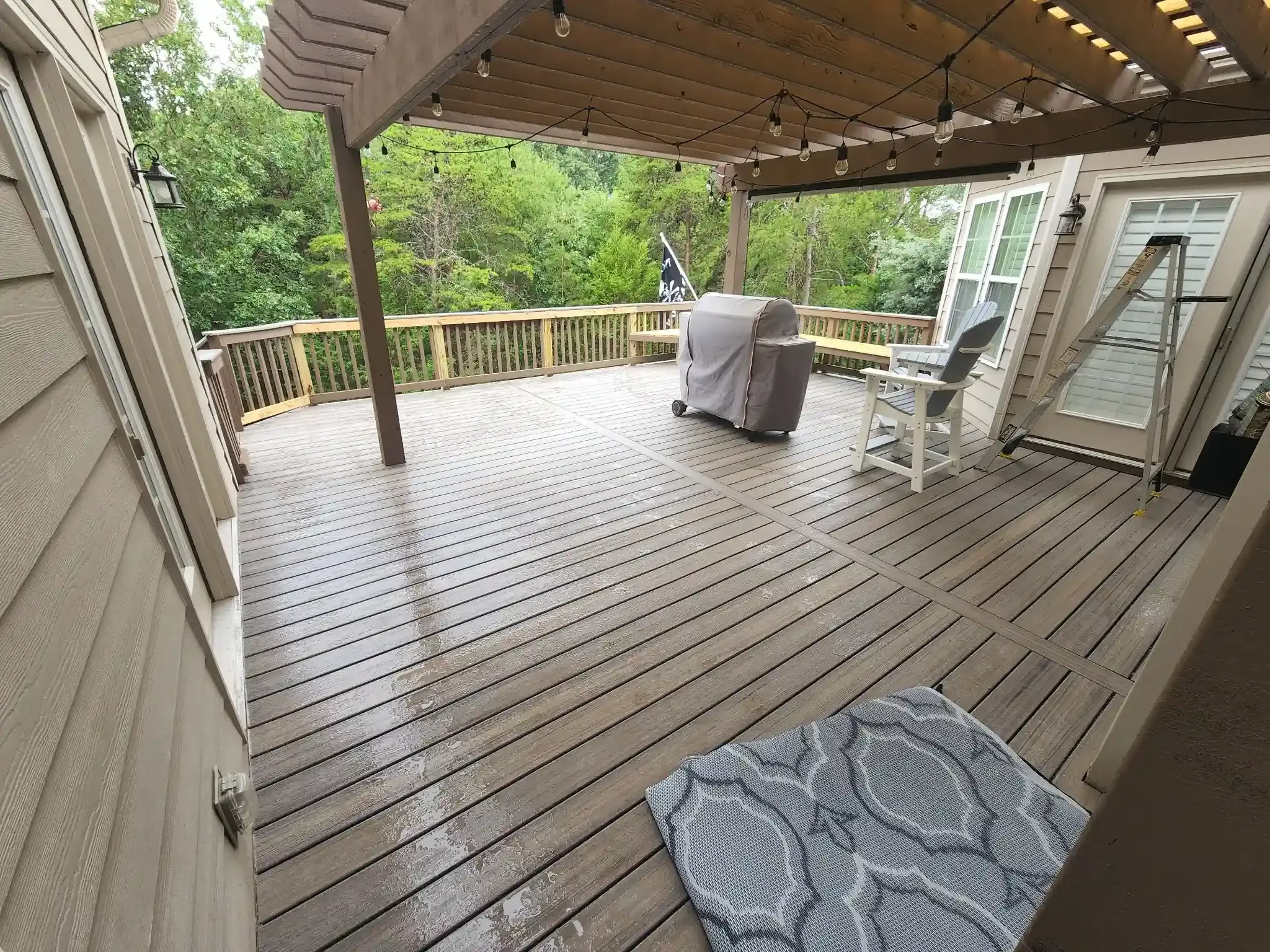 Wooden deck with pergola and grill, surrounded by trees. Includes a patterned rug and patio furniture.