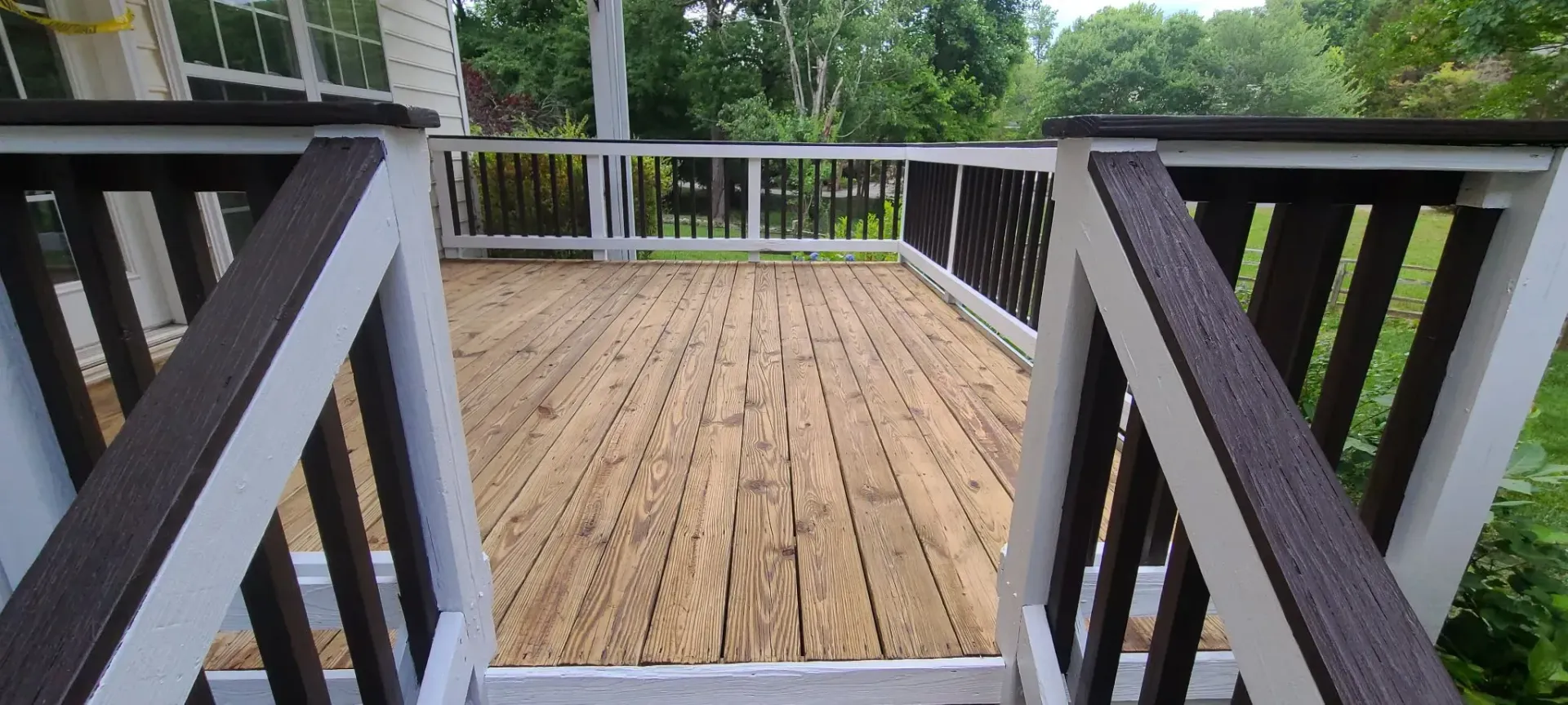 A weathered wooden deck with white and brown railings, surrounded by greenery.