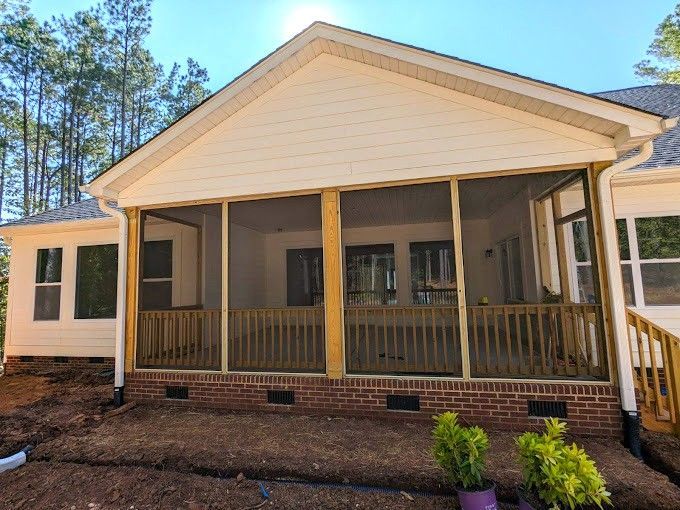 A newly constructed screened-in porch with a brick base, wooden posts, and railing, set against a backdrop of trees.