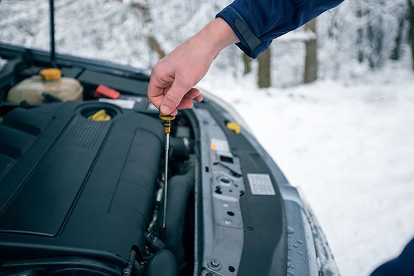 A person is checking the oil level of a car in the snow. | Autotrends - Irving Park