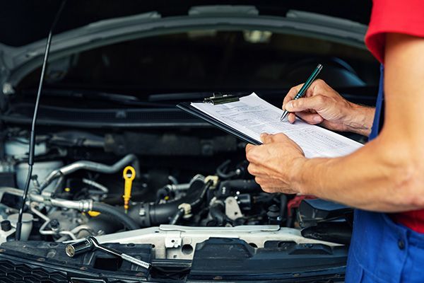 A mechanic is writing on a clipboard while working on a car. | Autotrends - Irving Park