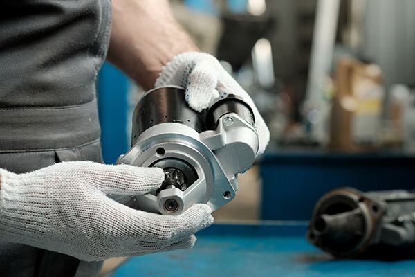 A man is holding a starter motor in his hands. | Autotrends - Irving Park