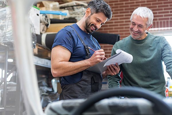 Two men are looking at a clipboard in a garage. | Autotrends - Irving Park