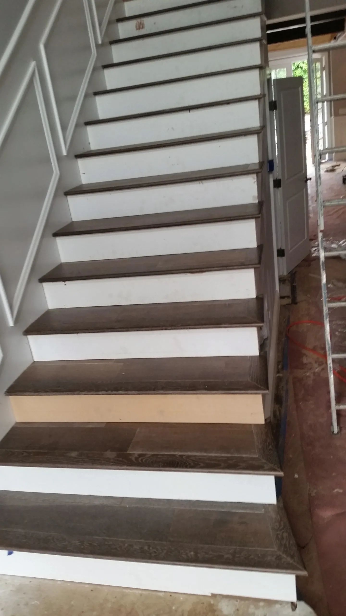 A wooden staircase with white steps and a ladder in the background