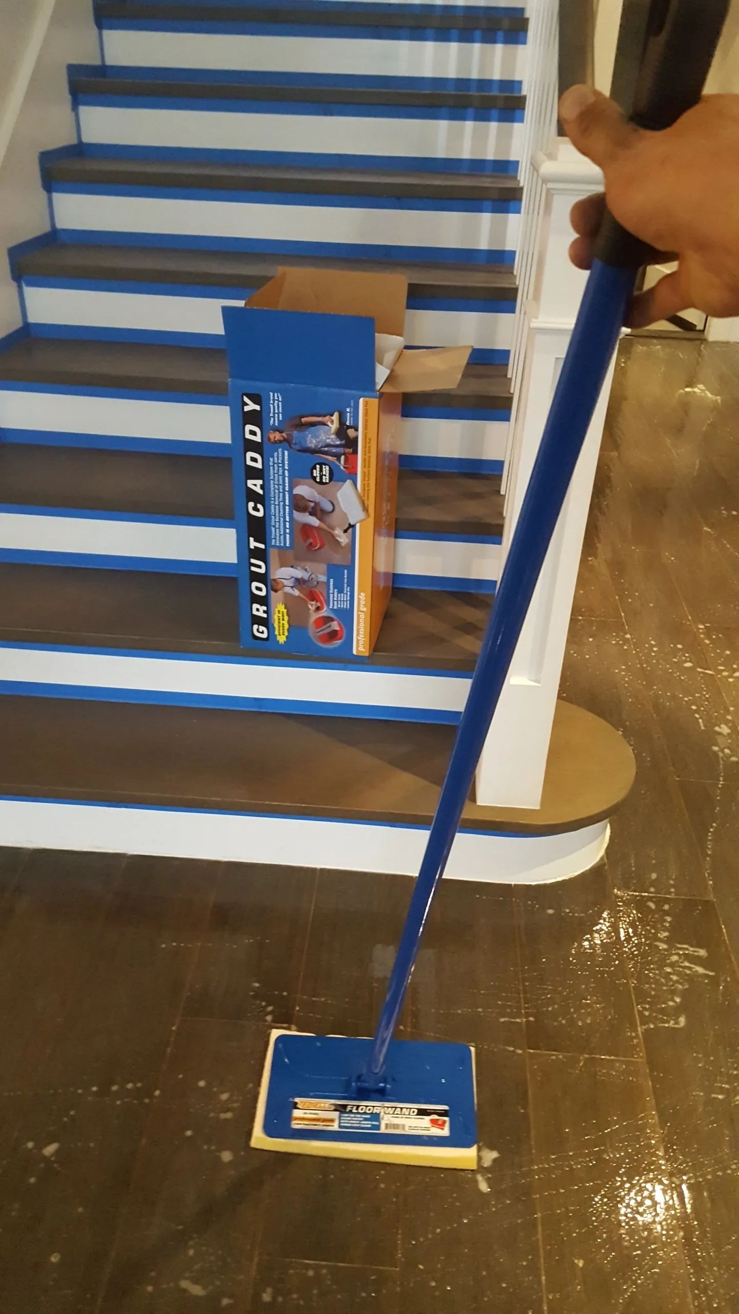 A person is holding a mop in front of a set of stairs