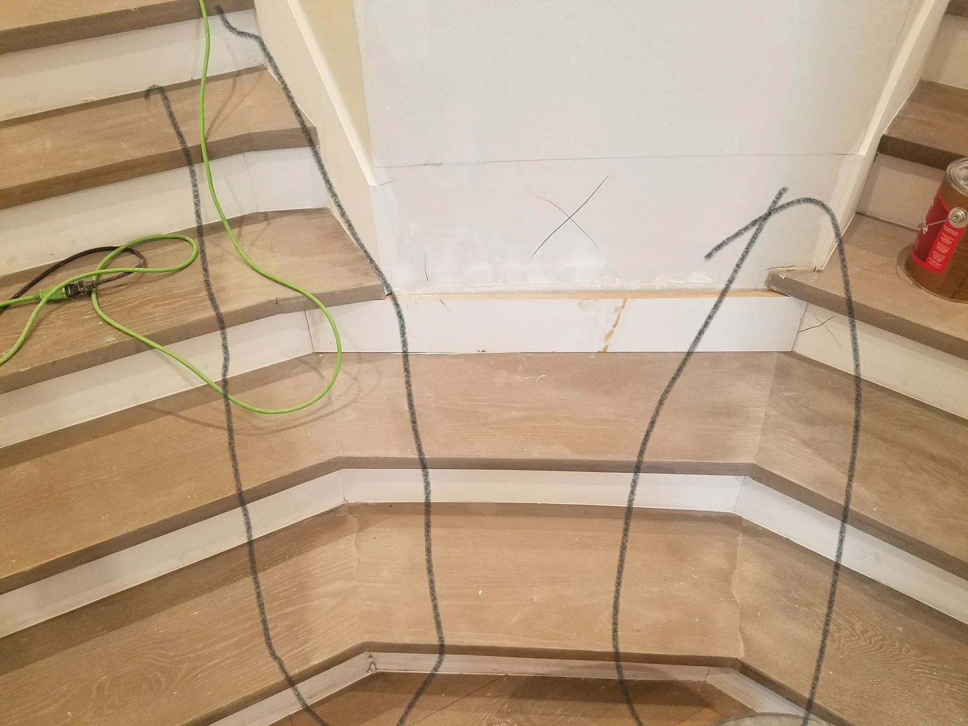A bunch of wires are hanging from the bottom of a wooden staircase