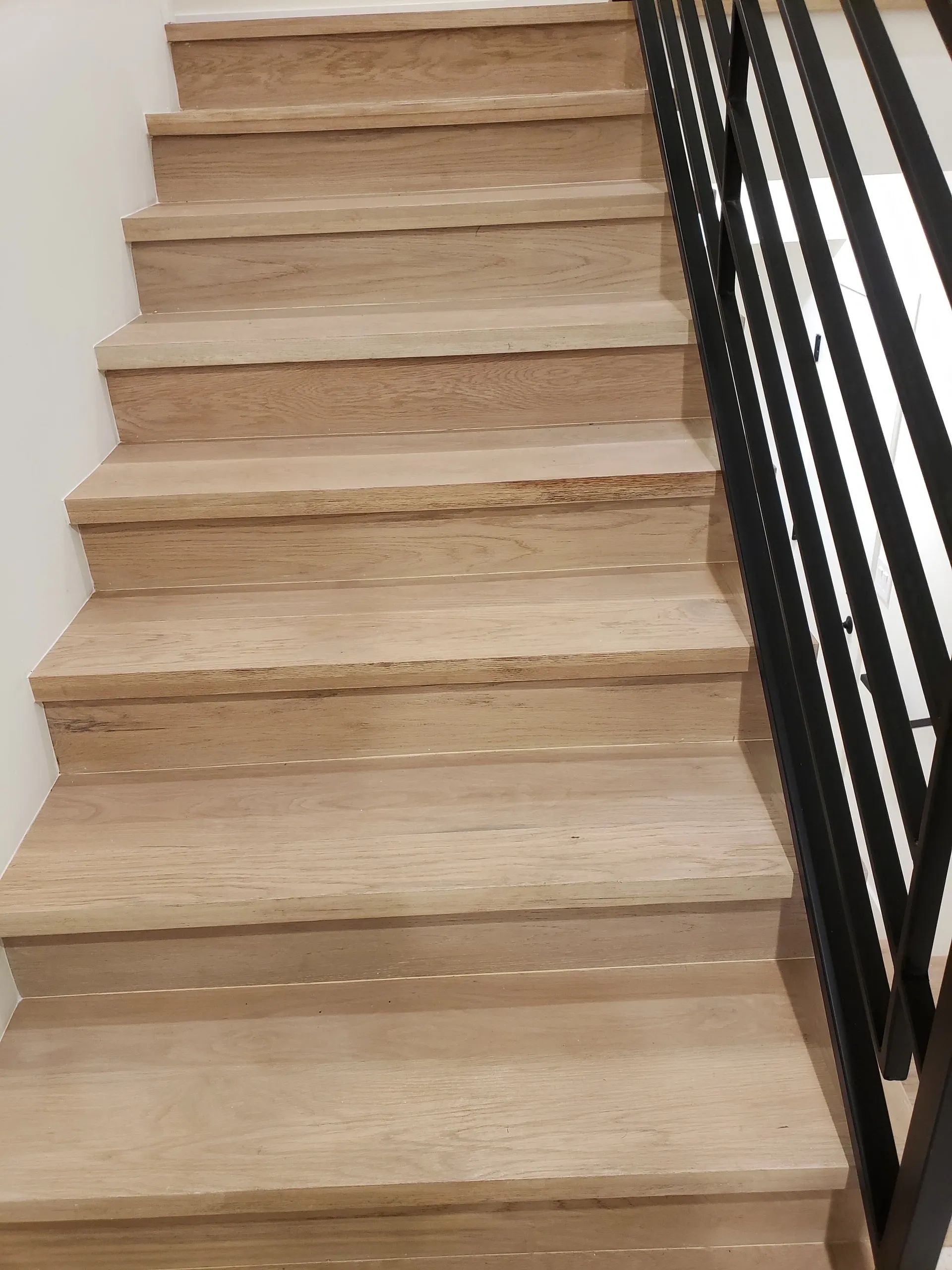 A set of stairs with a black railing and a white wall