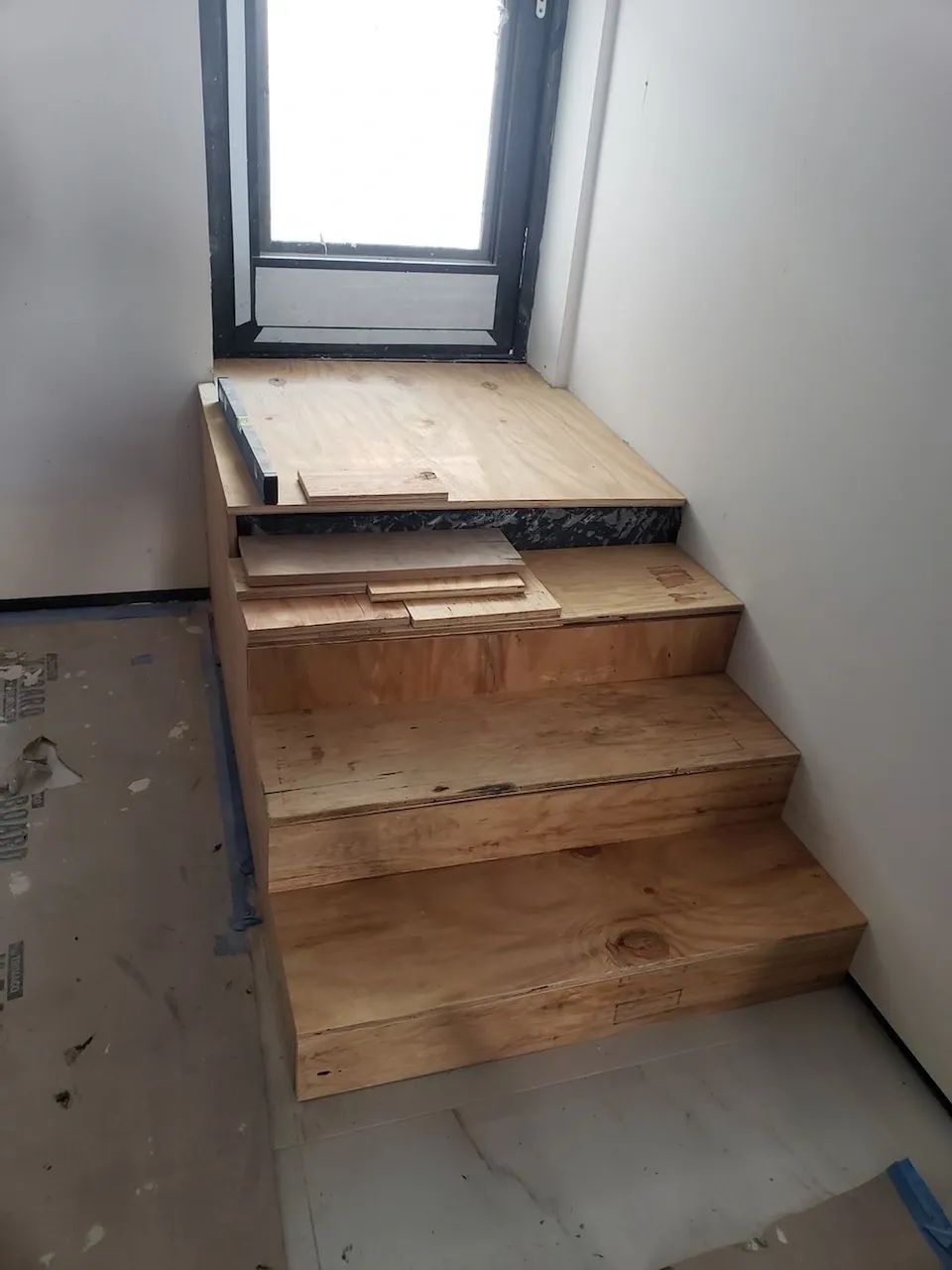 A wooden staircase is being built in a room next to a window