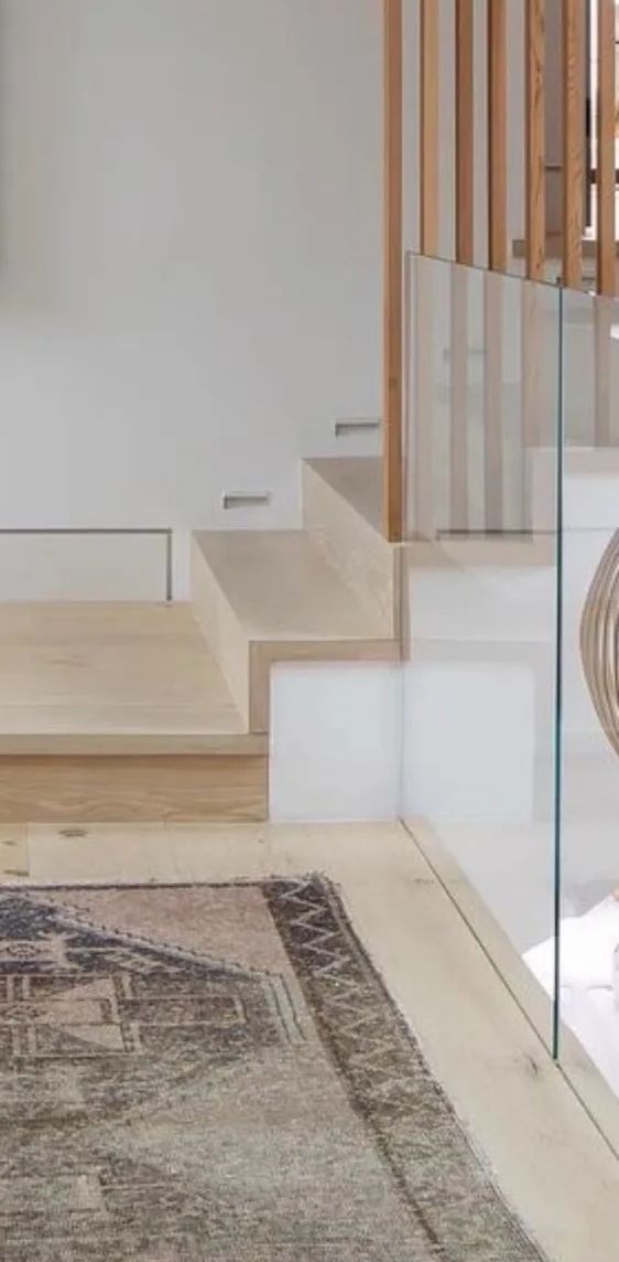 A wooden staircase with a glass railing and a rug on the floor