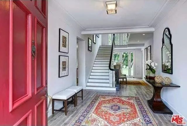 A hallway with a red door and stairs in the background