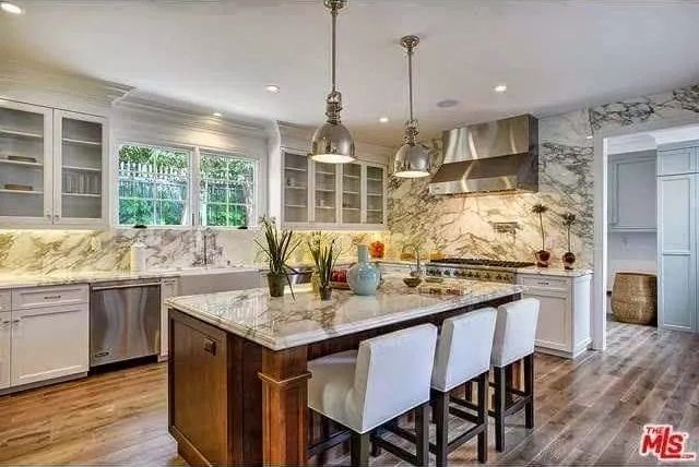 A kitchen with white cabinets, marble counter tops, stainless steel appliances and a large island