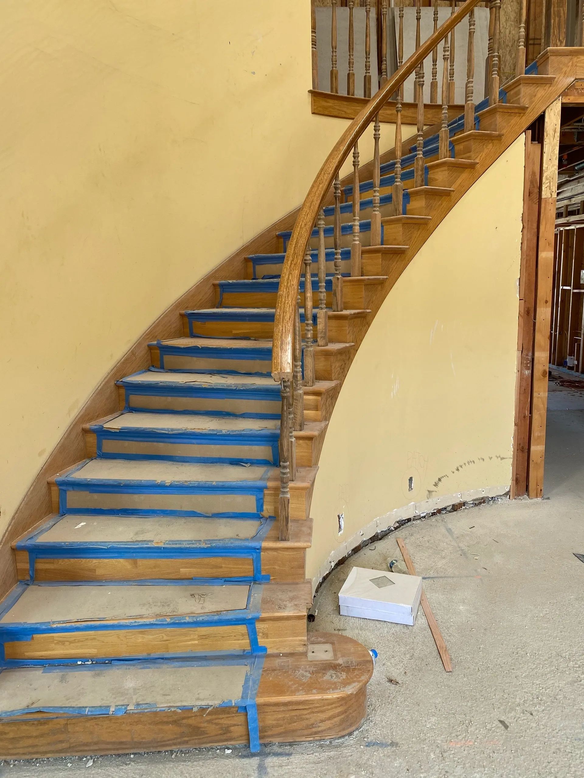 A curved wooden staircase with blue tape on the steps