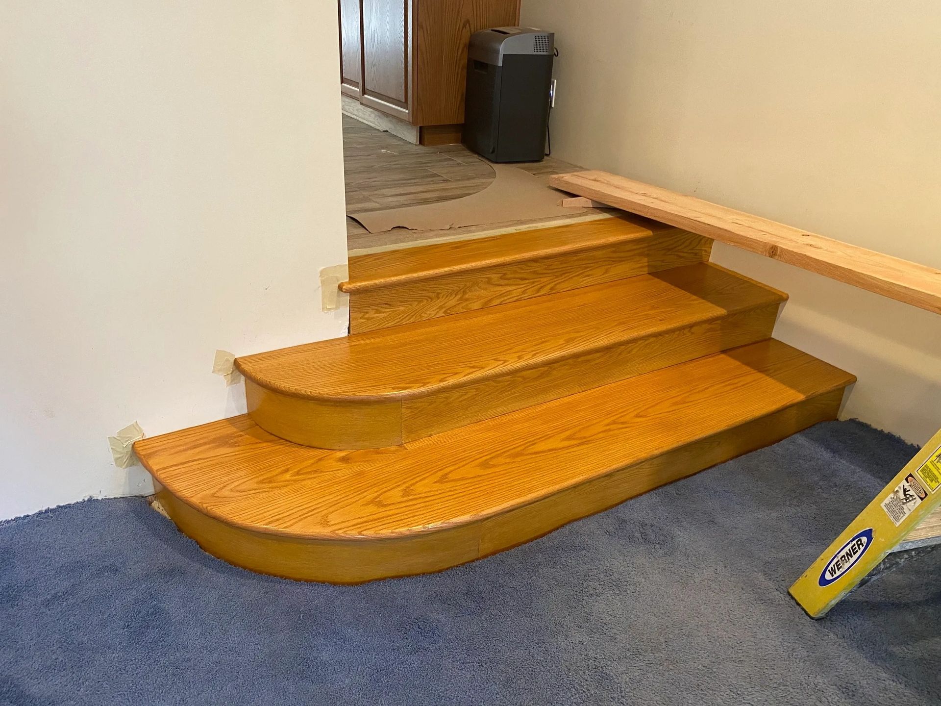 A set of wooden stairs in a room next to a yellow ladder