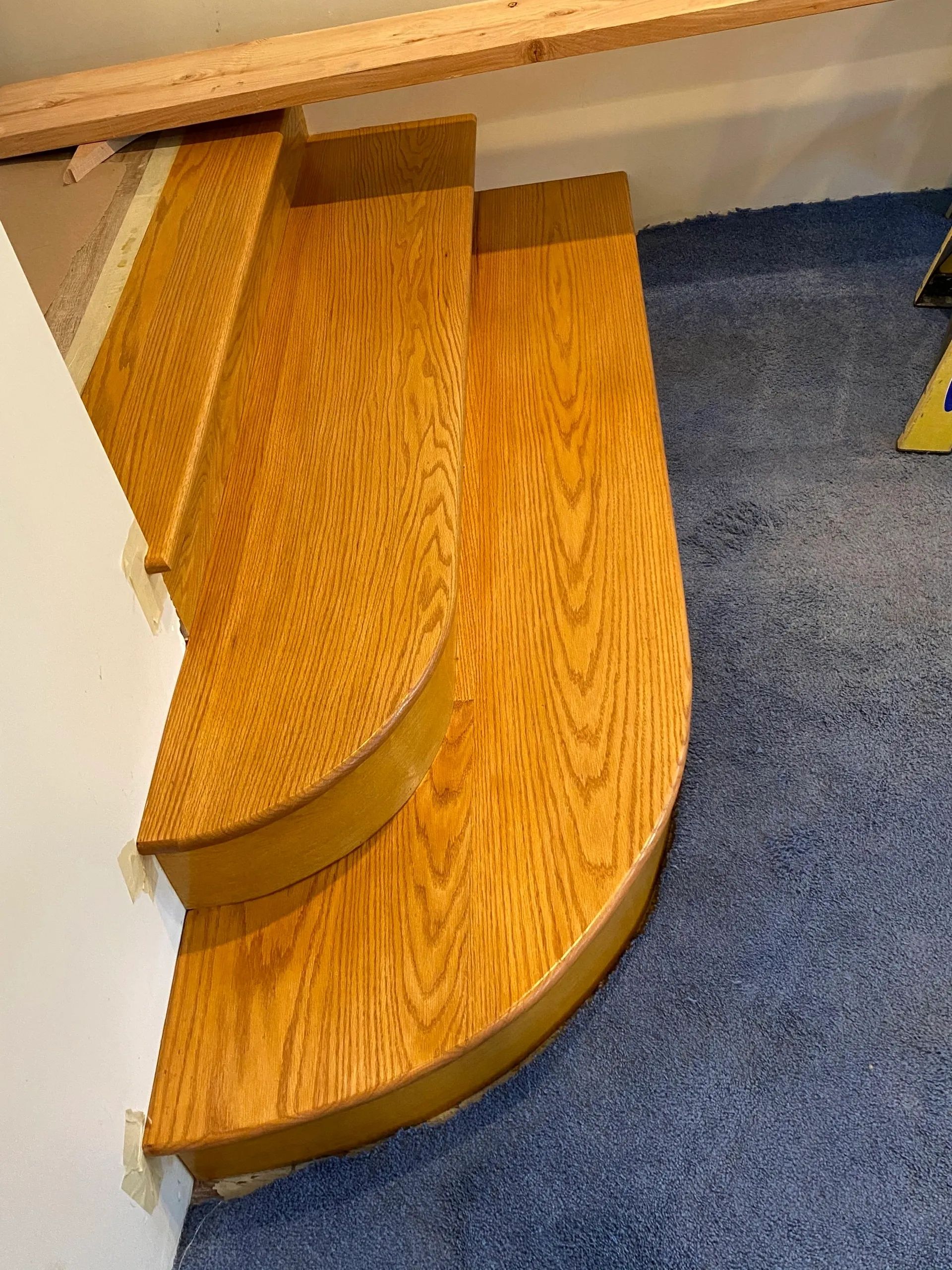 A wooden staircase is sitting on top of a blue carpeted floor