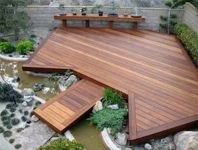 A wooden deck with a bridge over a pond in a garden