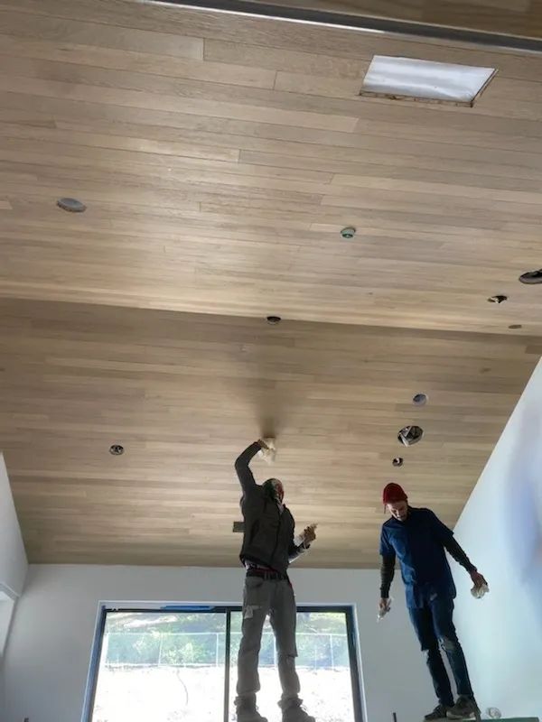 Two men are working on a wooden ceiling in a living room