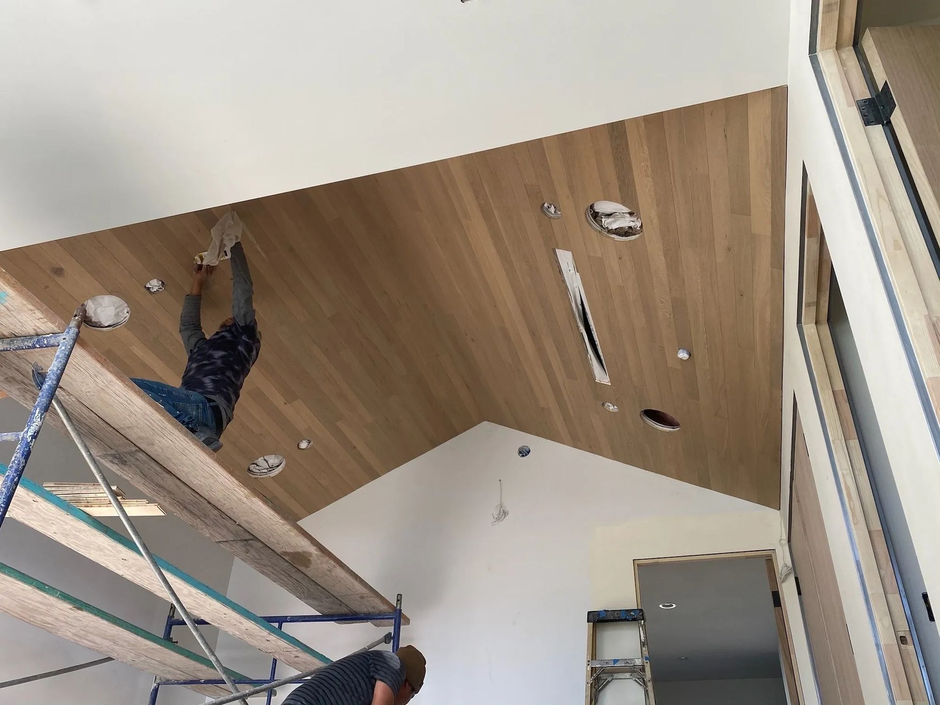 A man is working on a wooden ceiling in a room