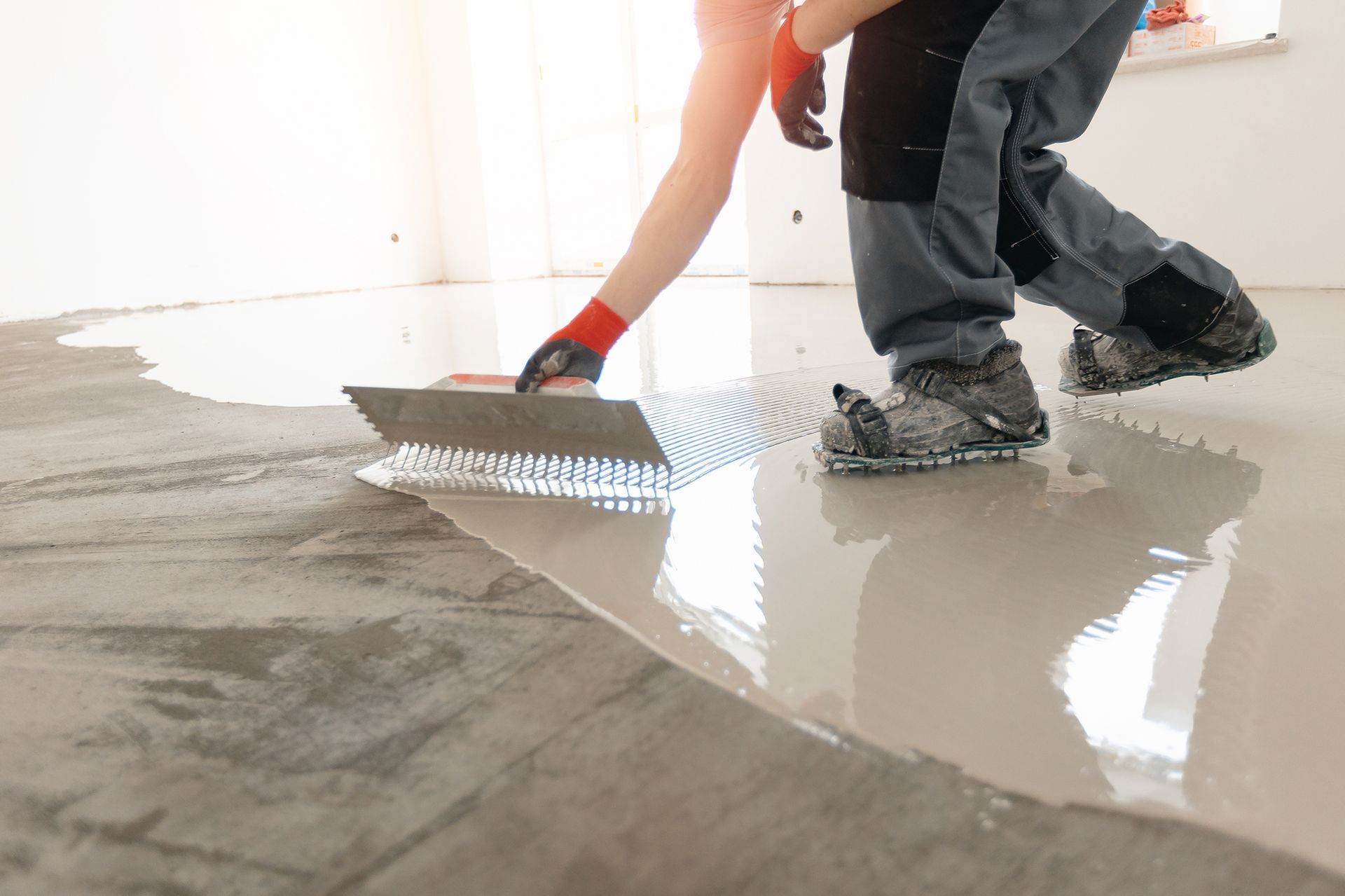 A man is spreading concrete on a floor with a trowel.