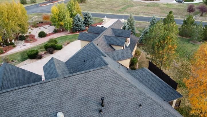Overhead view of a house with a complex, dark gray roof, trees, and a driveway.