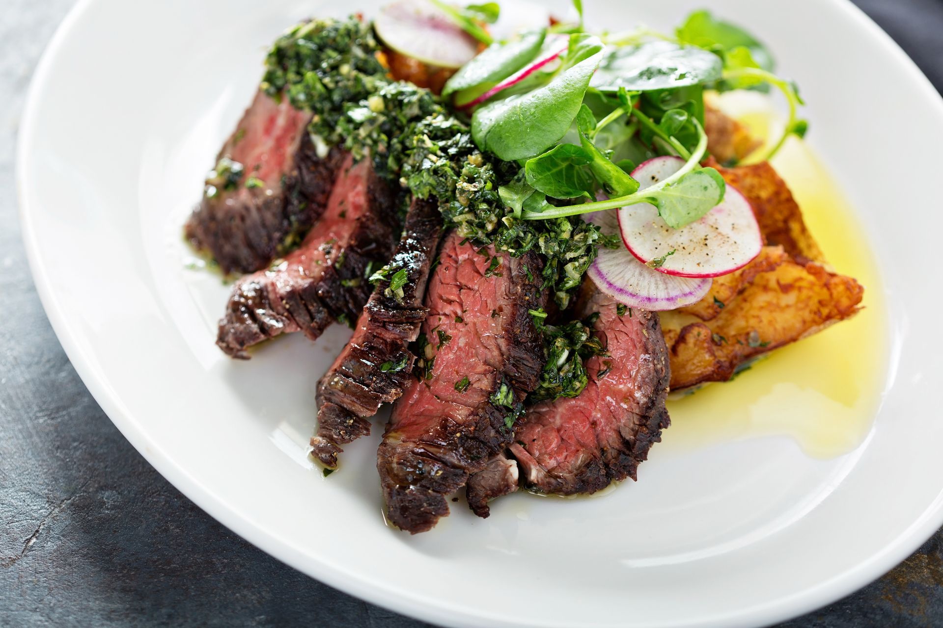 A white plate topped with steak , potatoes and vegetables.