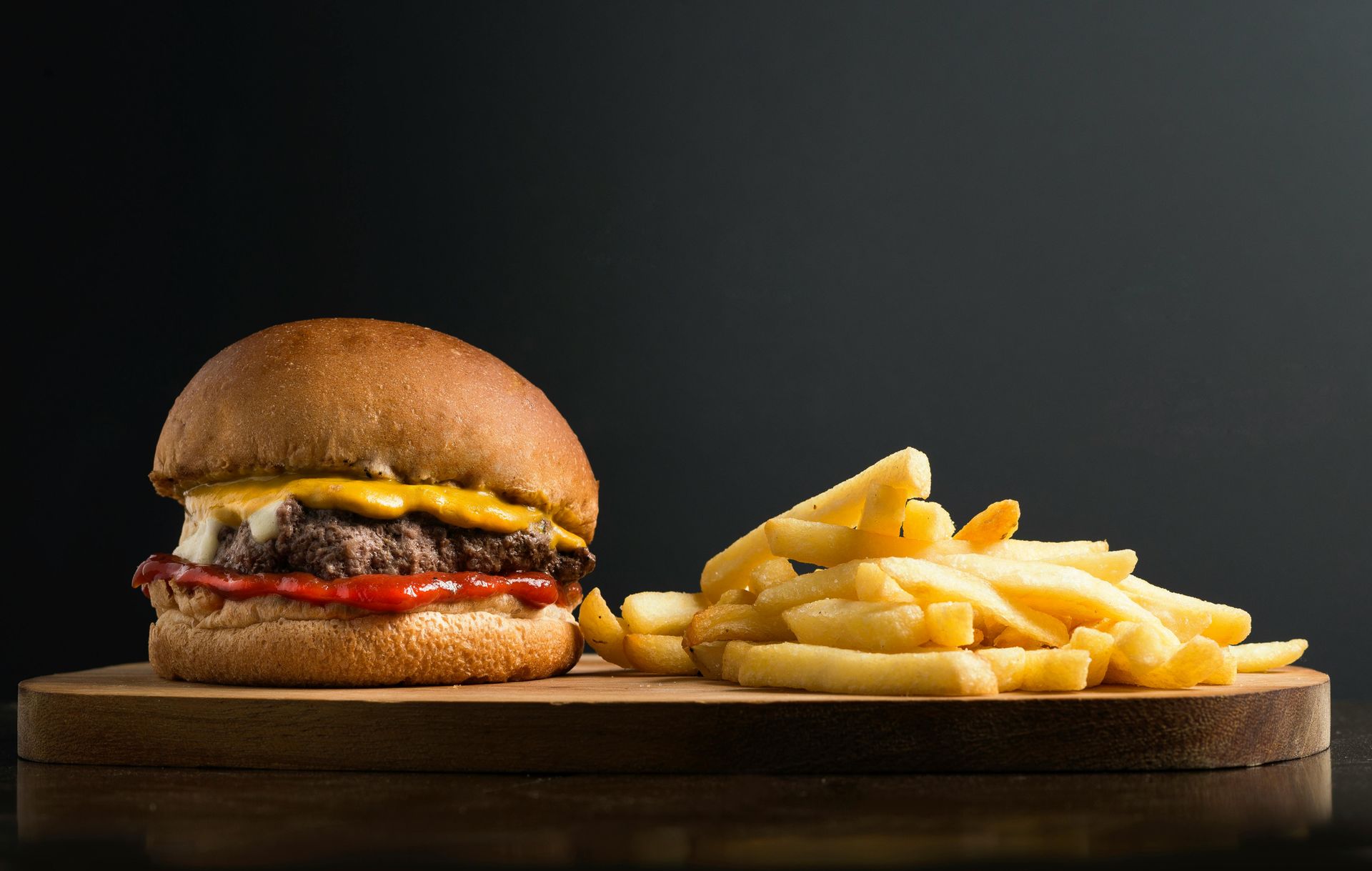 A hamburger and french fries on a wooden cutting board.