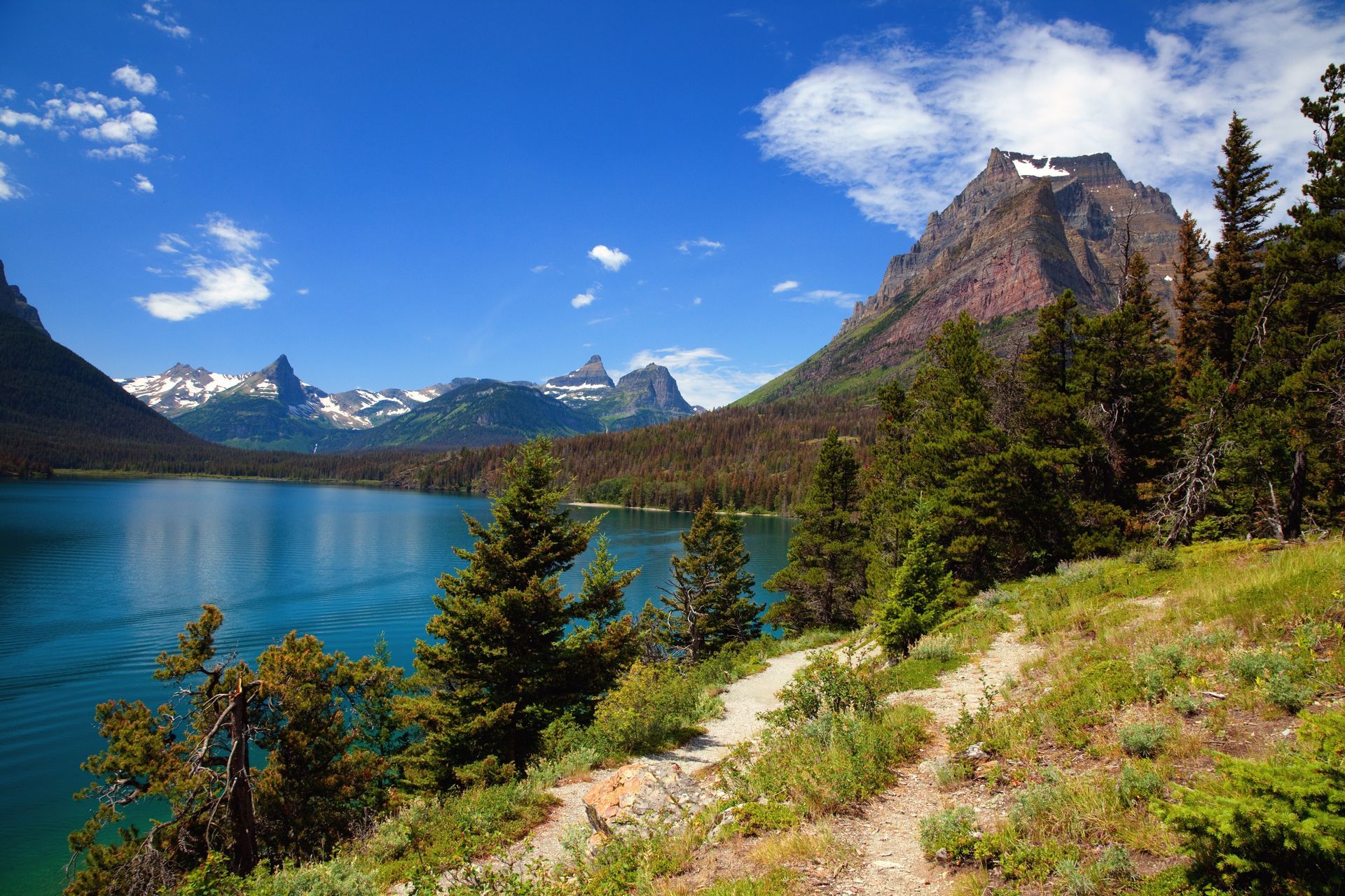 A lake surrounded by mountains and trees with a mountain in the background.