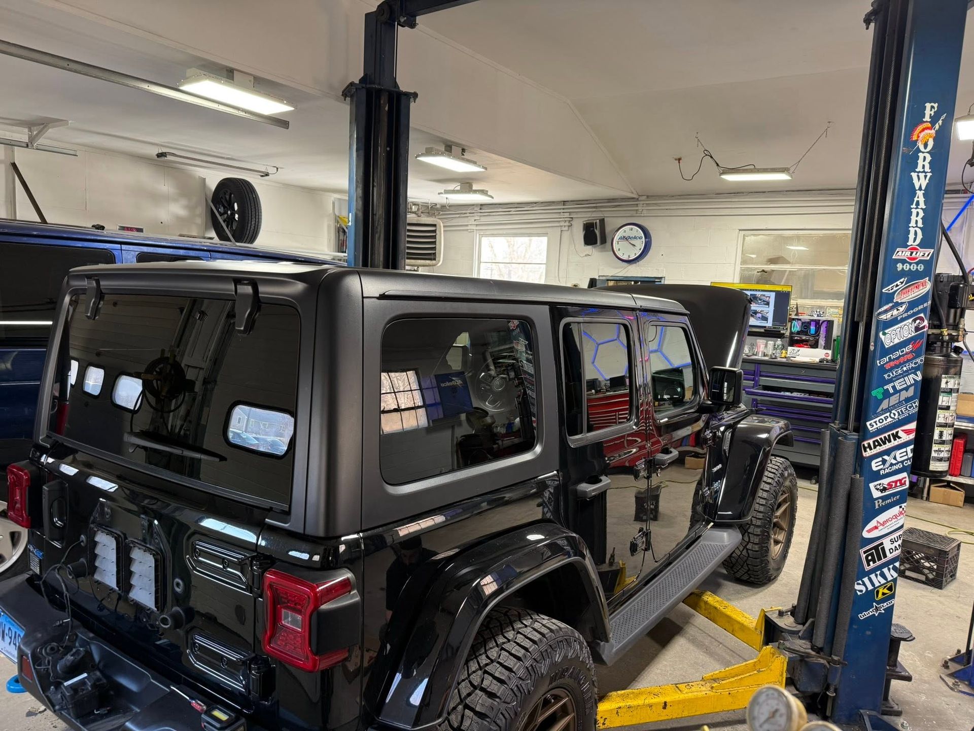 Black Jeep Wrangler on a lift inside an auto shop with another vehicle nearby
