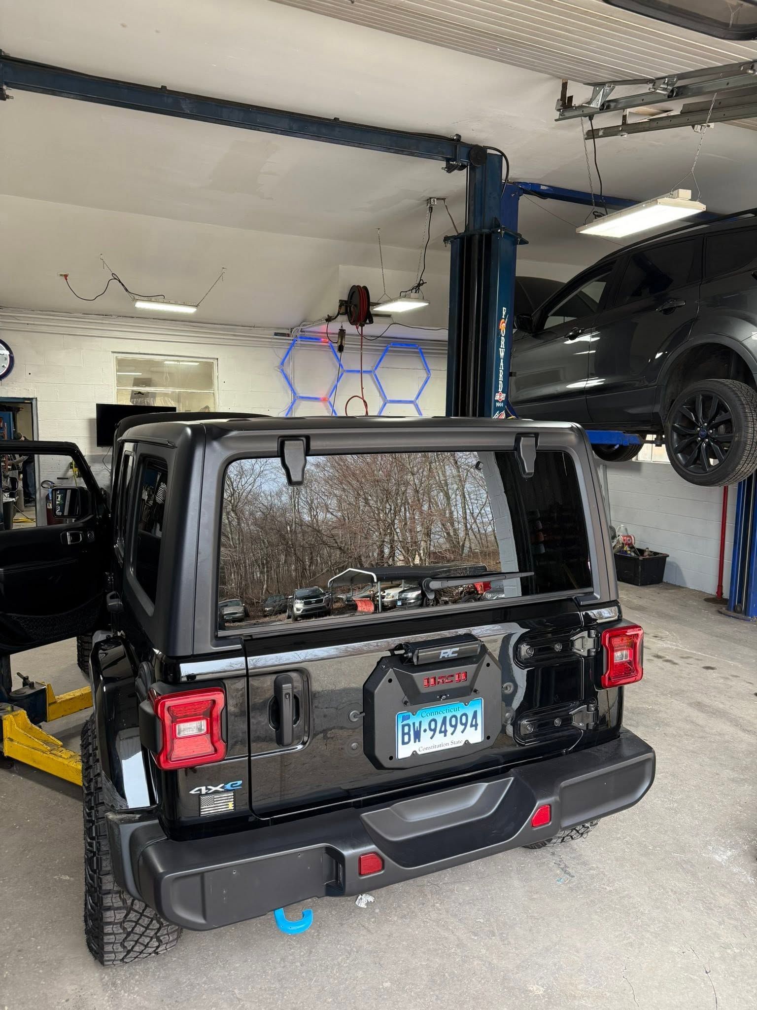 Black Jeep Wrangler in a garage on a car lift, with another vehicle raised above it.