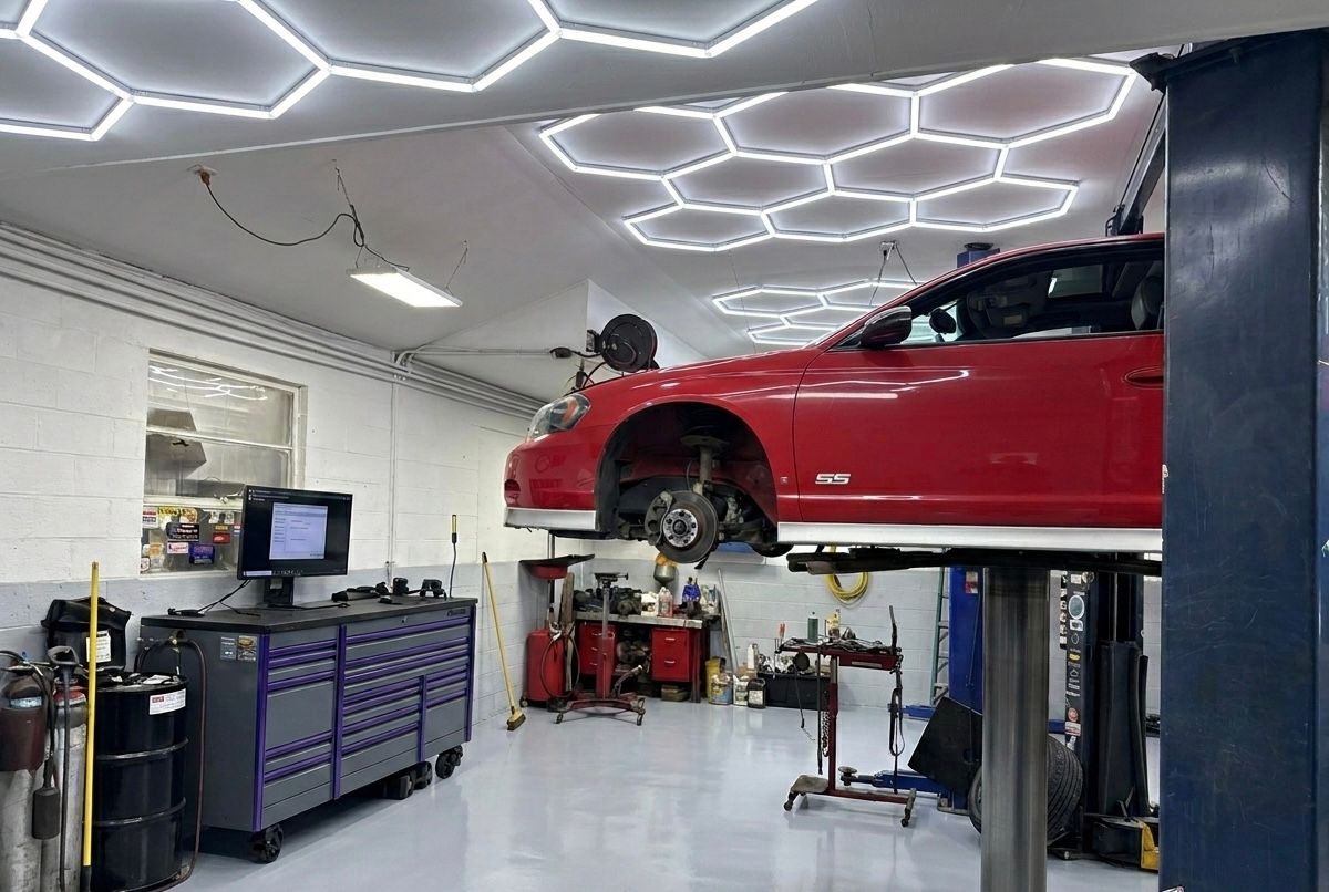 Red car lifted in a bright auto repair shop with tools, cabinets, and geometric LED ceiling lights.