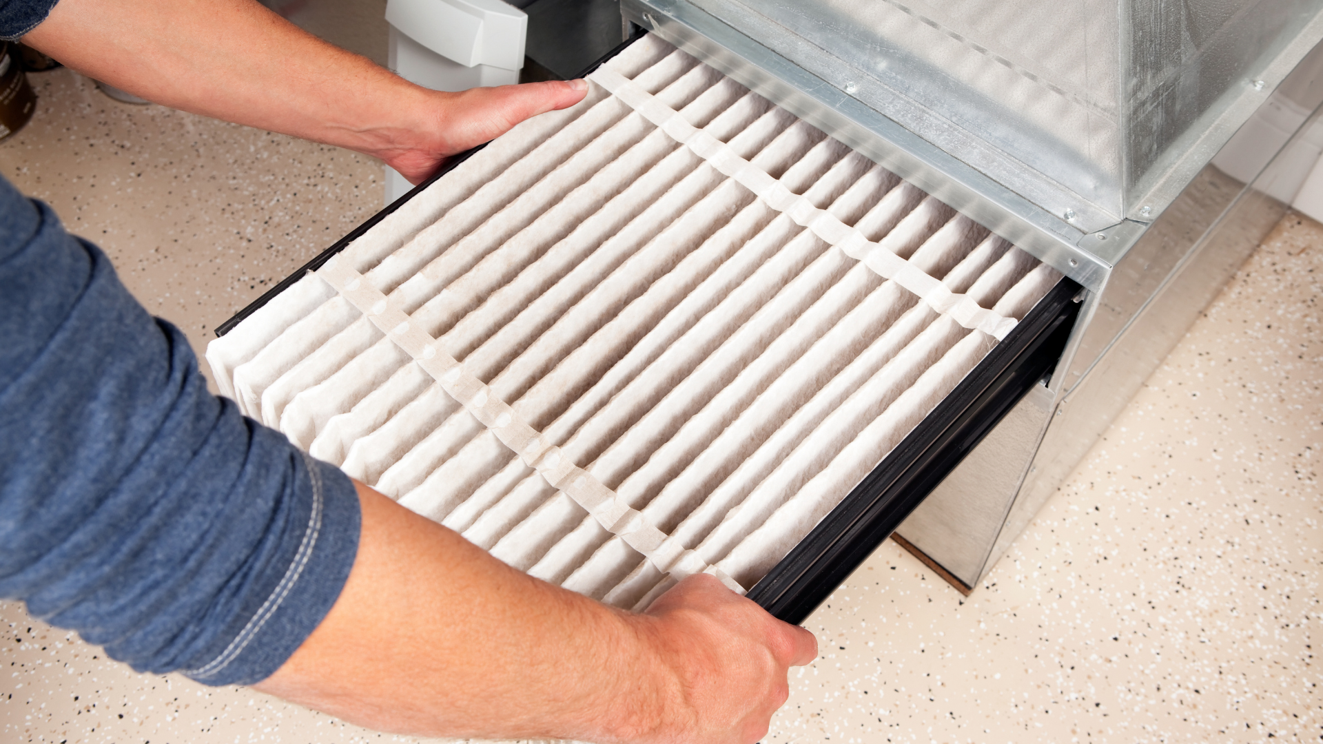 Person replacing an air filter in a metal housing, indoors. Filter is white, grid-like.