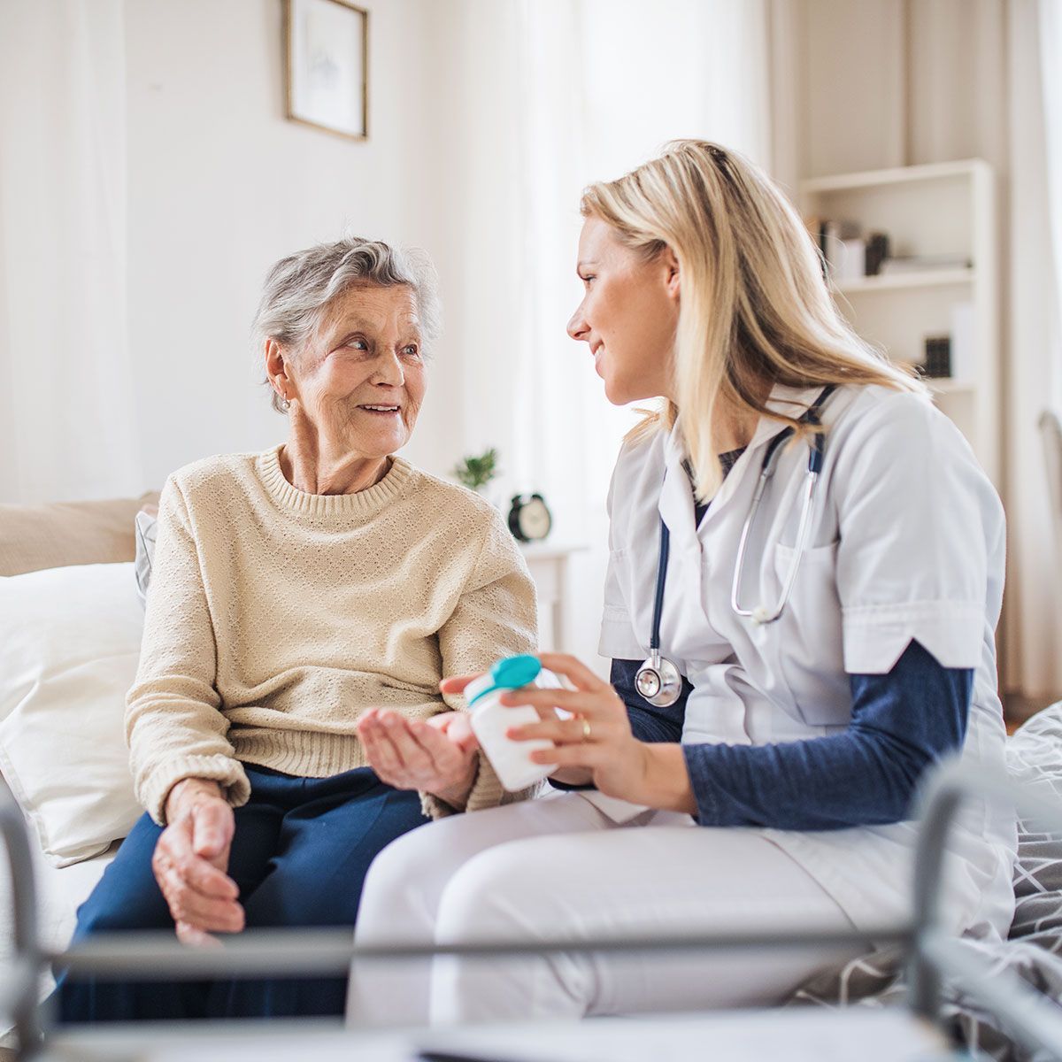 Nurse speaking with a patient in a bright home setting, holding a medication container.