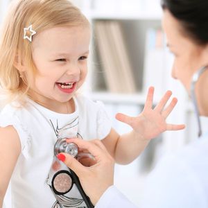 Doctor using a stethoscope to examine a smiling child in a bright clinic Doctor using a stethoscope to examine a smiling child in a bright clinic
