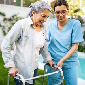 Woman helping an elderly man walk with a walker outdoors Woman helping an elderly man walk with a walker outdoors