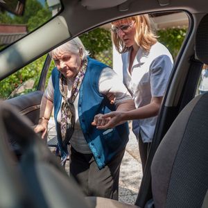Two people assisting someone into a car, viewed from the open front passenger door. Two people assisting someone into a car, viewed from the open front passenger door.